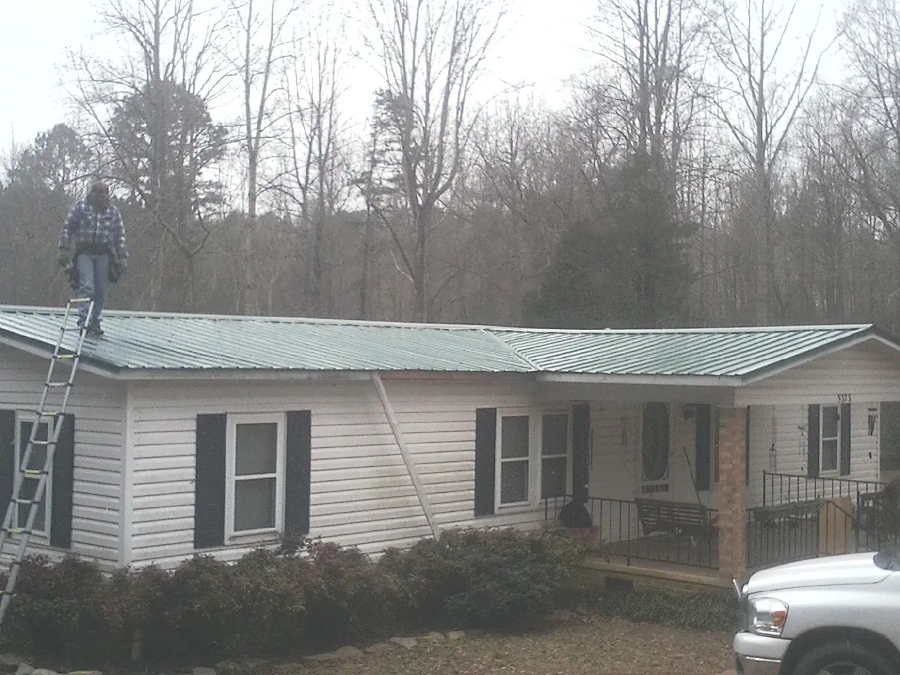 Worker on a ladder beside a new green metal roof on a ranch home in Elgin